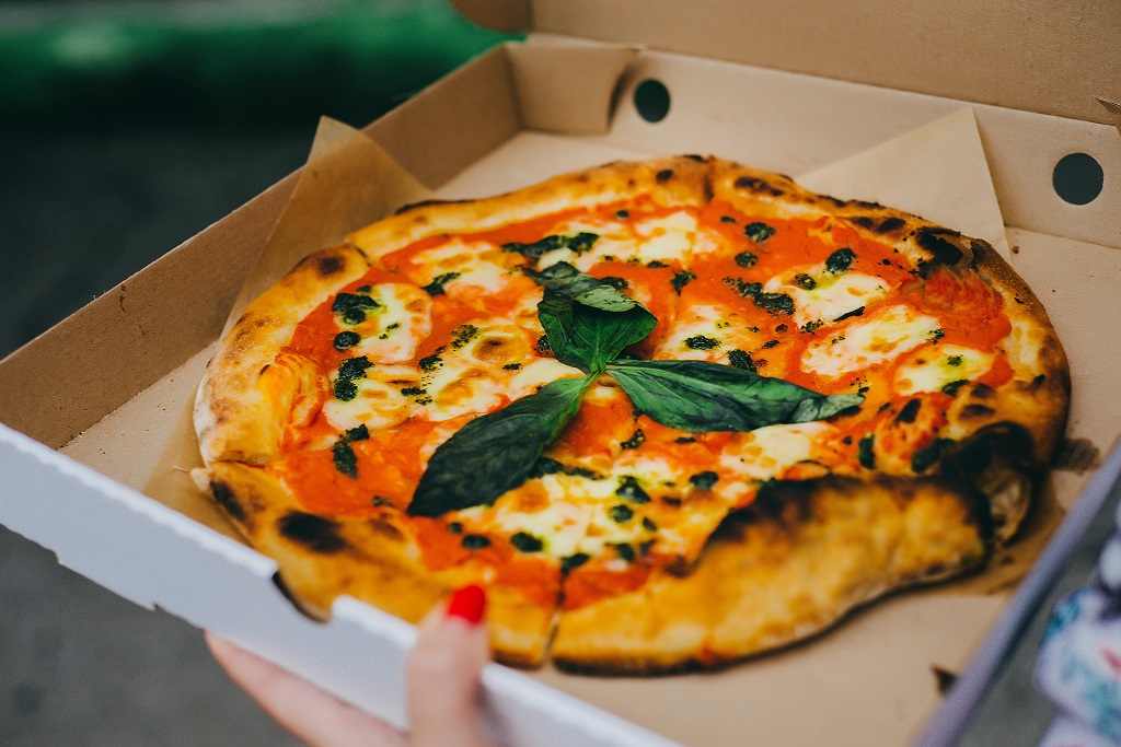 A whole pizza in a cardboard box with three green leaves as garnish