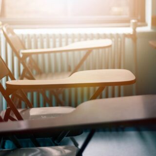 Image of the desk and seat part of three beige/brown desk chairs with half-desktops in a row, lit by light from the back/top of the scene.