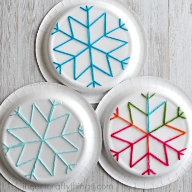 Three white paper plates each with a snowflake design made of yarn