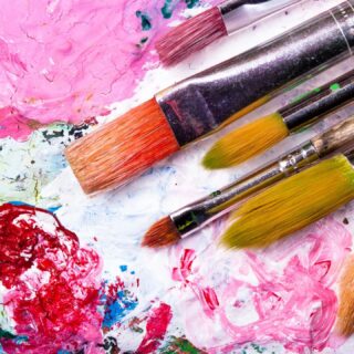 Five artists paintbrushes on a white background surrounded with splashes of hot pink and light pink